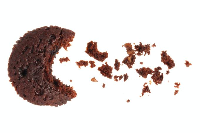 Crescent shaped chocolate cake, with crumbs to its right, all on a white background