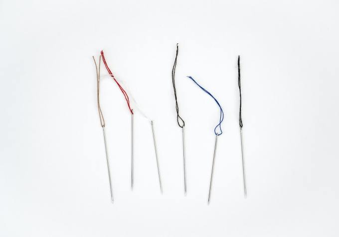 Six sewing needles, each with a different colored thread, on a white background