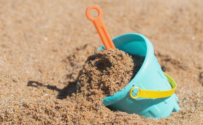 A light blue plastic pail filled with sand on the beach.