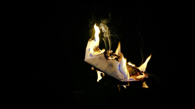 Paper boat on fire against a black backdrop