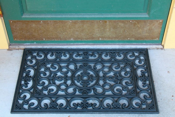 black doormat beneath a teal door
